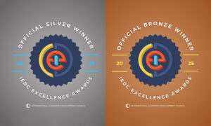 Two award badges side by side: on the left, a gray background with the text ‘Official Silver Winner – IEDC Excellence Awards 2025’; on the right, a bronze background with the text ‘Official Bronze Winner – IEDC Excellence Awards 2025’. Both feature the International Economic Development Council logo in the center.